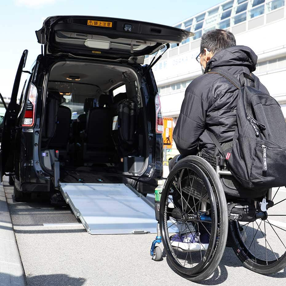 Usuario de silla de ruedas subiendo a un taxi universal por la rampa trasera.